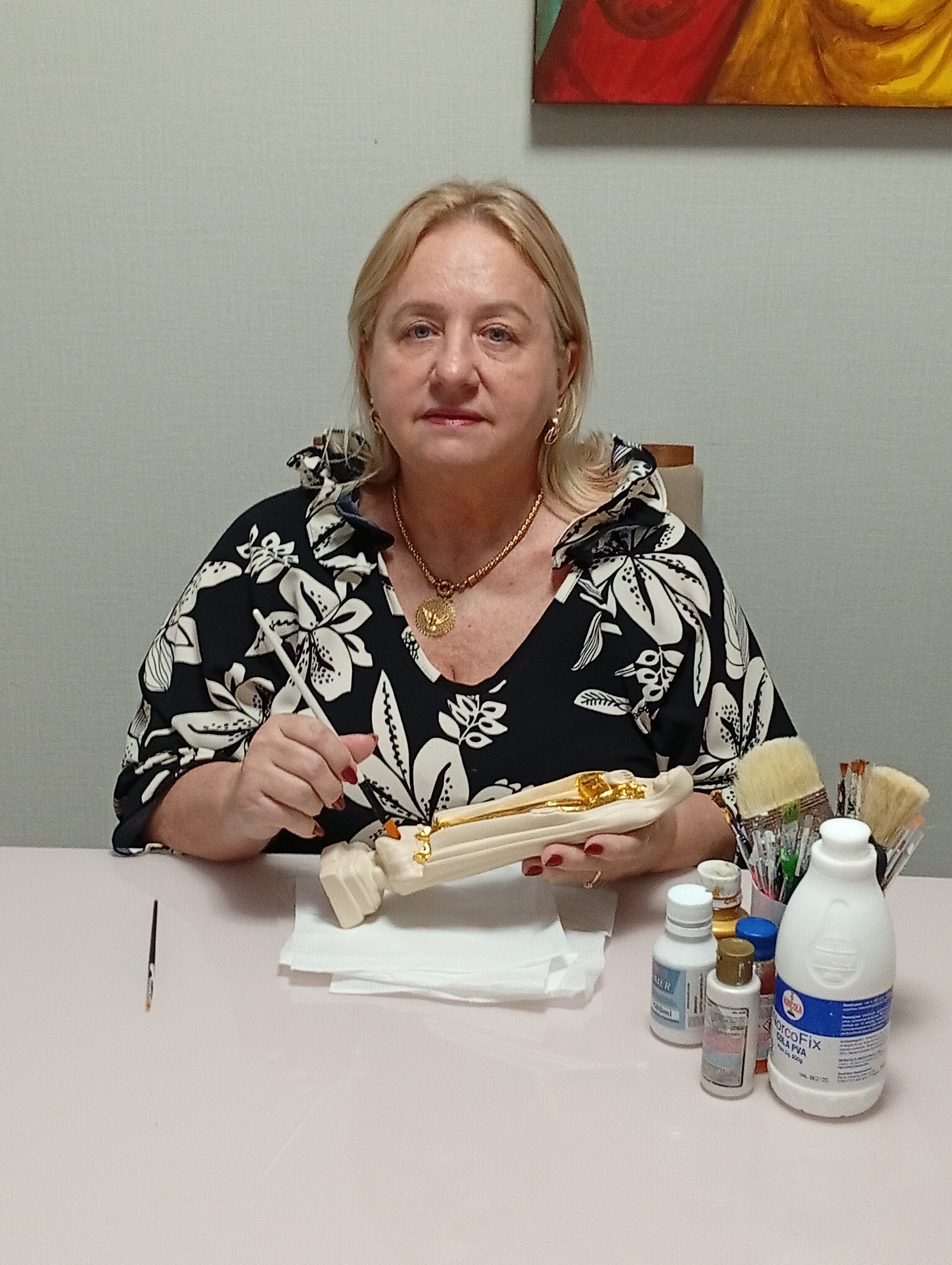 Socorro Dias pintando uma peça artesanal com detalhes dourados